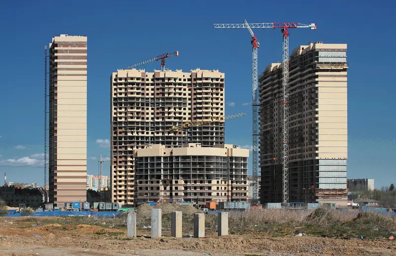 Torres residenciais em construção com guindastes, ao lado de prédios já prontos