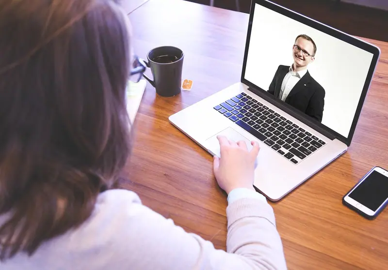 Pessoa de costas, sentada à mesa, participando de uma videochamada no notebook