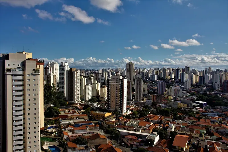Prédios residenciais e telhados de casas de uma grande cidade brasileira, sob céu azul com nuvens