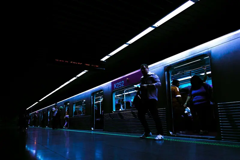 Trem do metrô parado na plataforma à noite, com passageiros embarcando