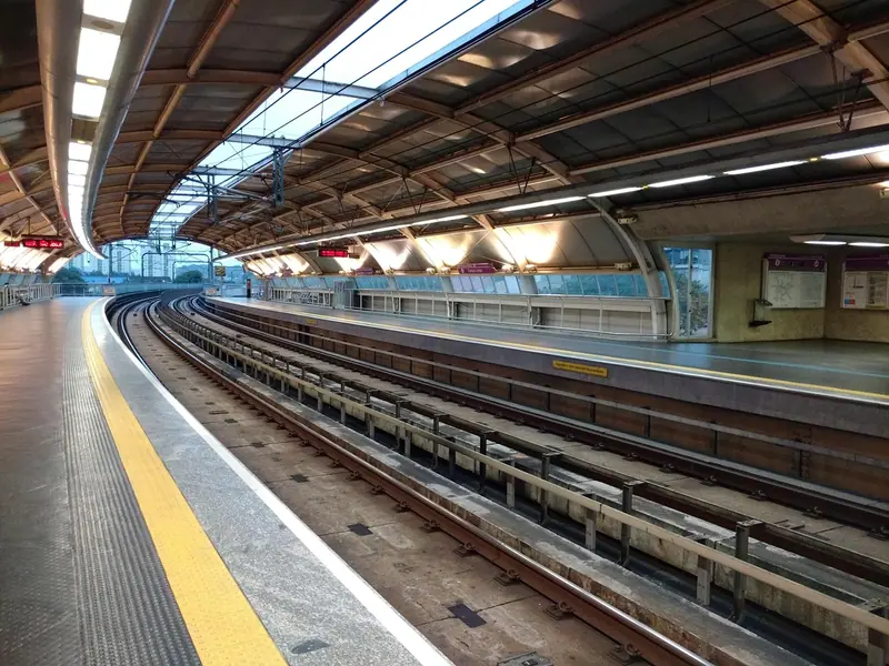 Plataforma vazia de uma estação de trem, com a faixa amarela e os trilhos fazendo uma curva