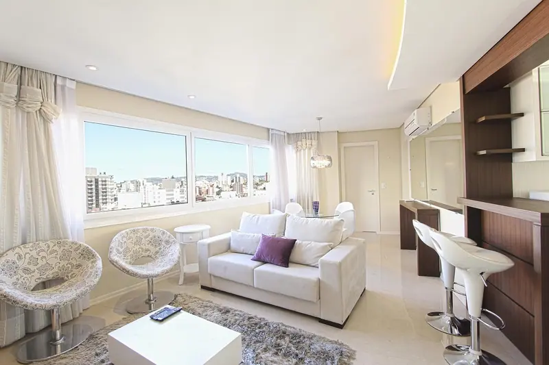 Sala de apartamento clara, com sofá branco e janelas largas voltadas para prédios da cidade