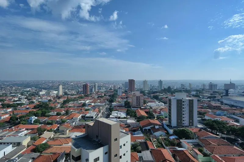 Telhados de casas e sobrados vistos do alto, com alguns prédios no meio e céu azul ao fundo