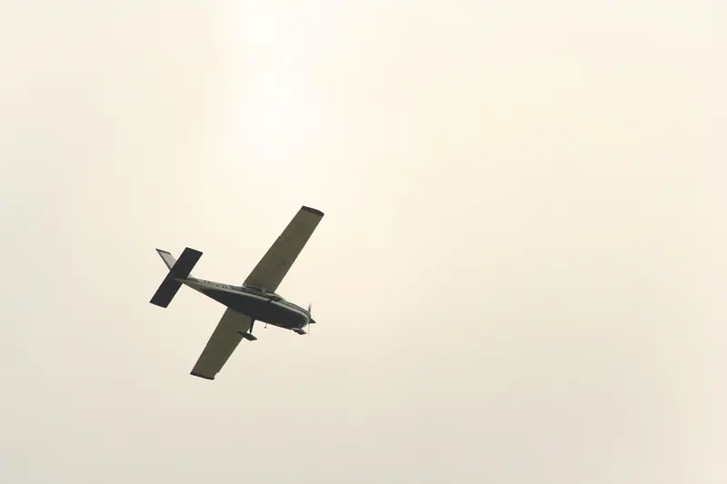 Avião pequeno de hélice em voo, visto de baixo contra o céu claro