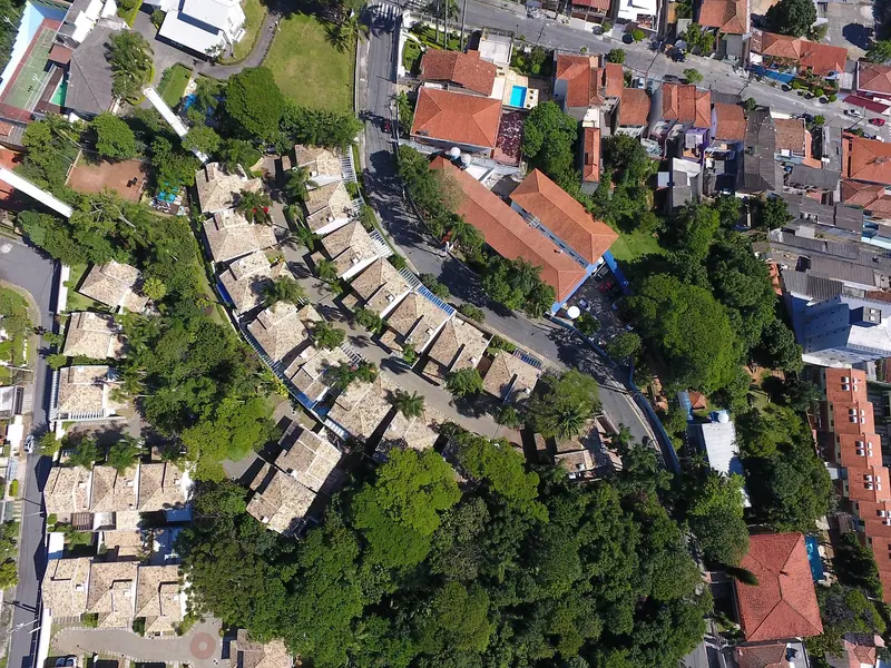 Vista aérea de um bairro com casas de telhado, ruas arborizadas e prédios ao lado