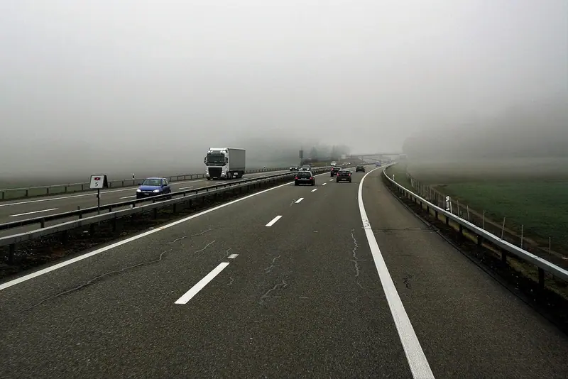 Estrada larga com caminhão e carros passando numa manhã de neblina