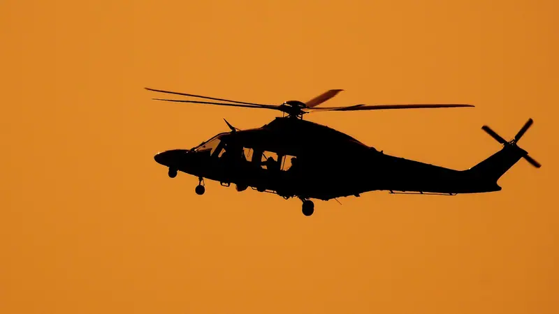 Silhueta escura de um helicóptero em voo contra o céu alaranjado