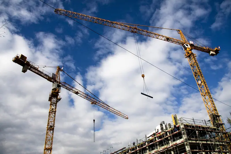 Dois guindastes amarelos sobre um prédio em construção, com céu azul e nuvens