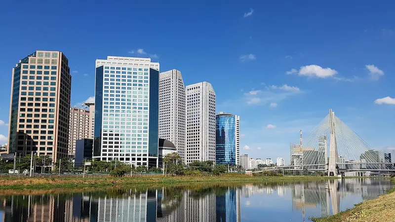 Rio Pinheiros com prédios comerciais na margem refletidos na água, sob céu azul