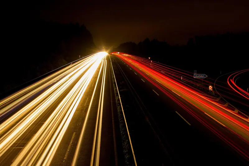 Rodovia à noite com rastros de luz dos faróis e lanternas dos carros