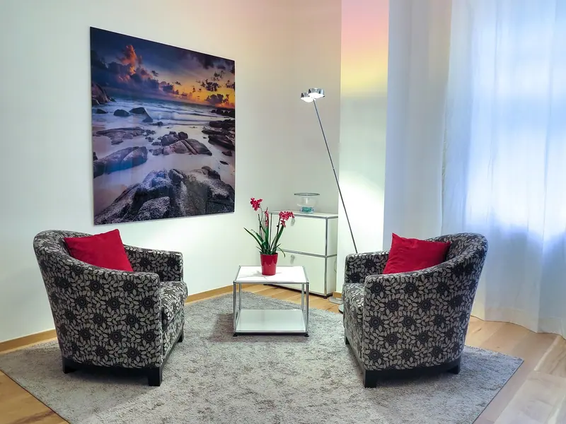Sala clara com duas poltronas, mesinha e cortina leve diante de uma janela