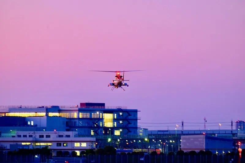 Helicóptero voando ao entardecer sobre um prédio iluminado, com o céu em tons de lilás