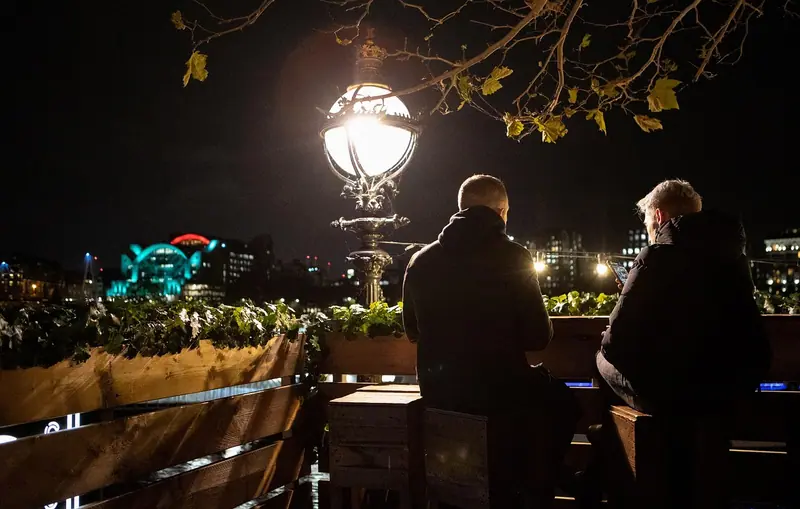 Duas pessoas de costas conversando num terraço à noite, sob a luz de um poste