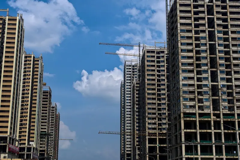 Torres residenciais altas em construção, com gruas ao lado, contra o céu azul com nuvens