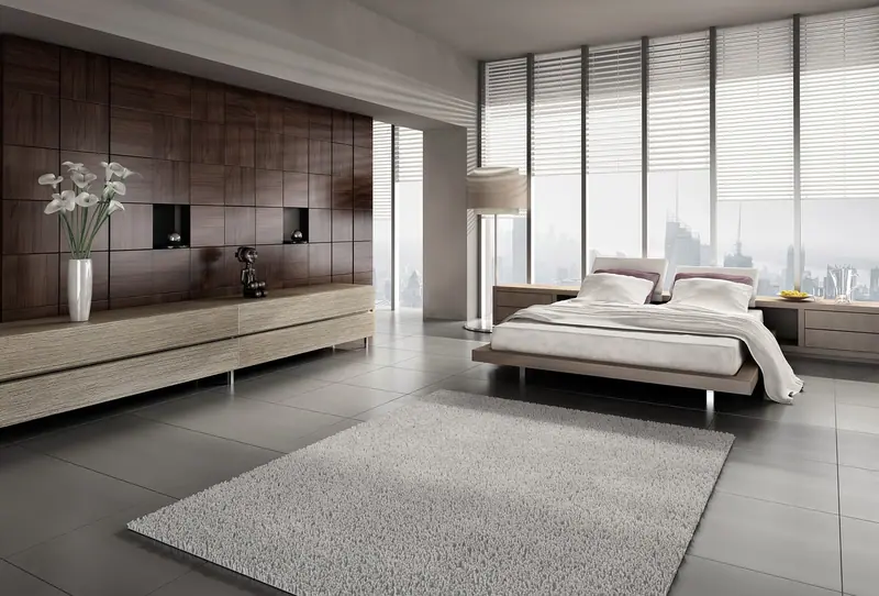 Quarto amplo e claro, com cama baixa, tapete felpudo e janela grande com persianas para a cidade