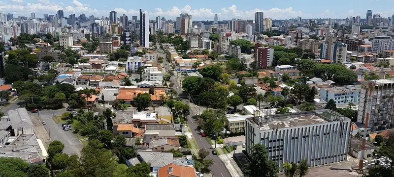 Vista do alto de um bairro com casas, prédios e muitas árvores, com torres no horizonte