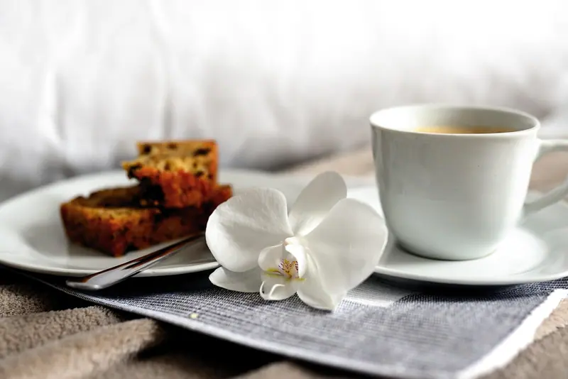 Xícara de café, bolo e uma orquídea branca numa bandeja sobre a cama
