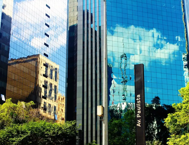 Placa da Avenida Paulista diante de prédios com fachada espelhada que refletem o céu