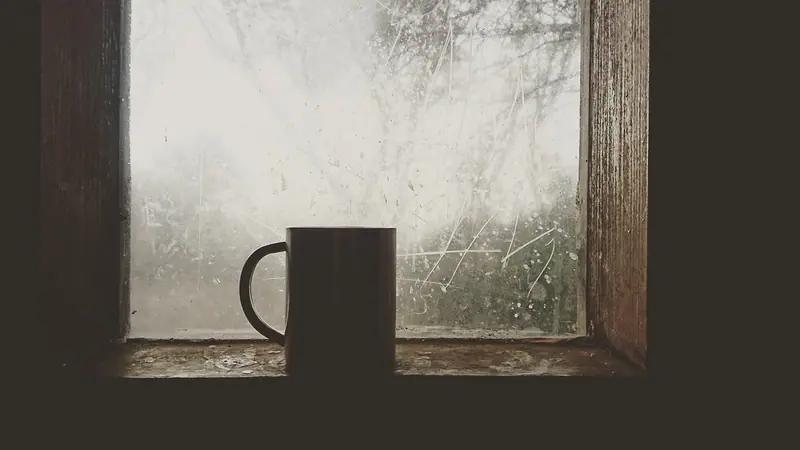 Caneca escura sobre o peitoril de uma janela de madeira com o vidro embaçado