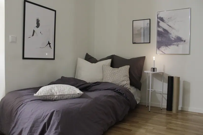 Quarto simples com cama arrumada, almofadas, quadros na parede e luz suave