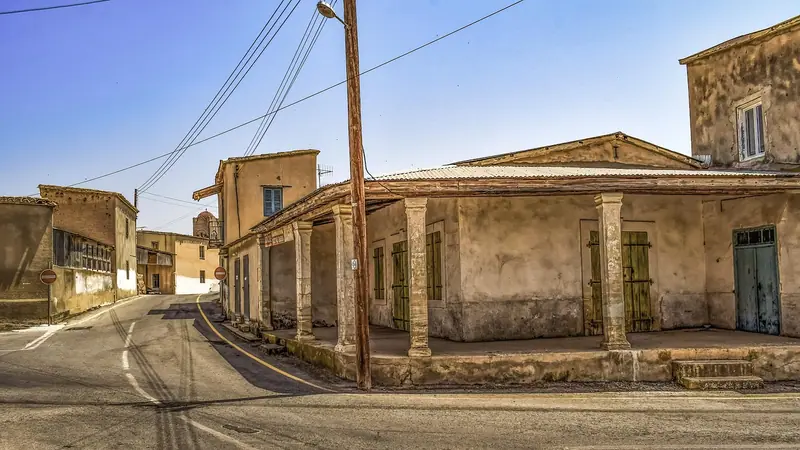 Casa antiga de paredes claras e varanda com colunas numa esquina onde a rua faz curva, com um poste de fios na calçada