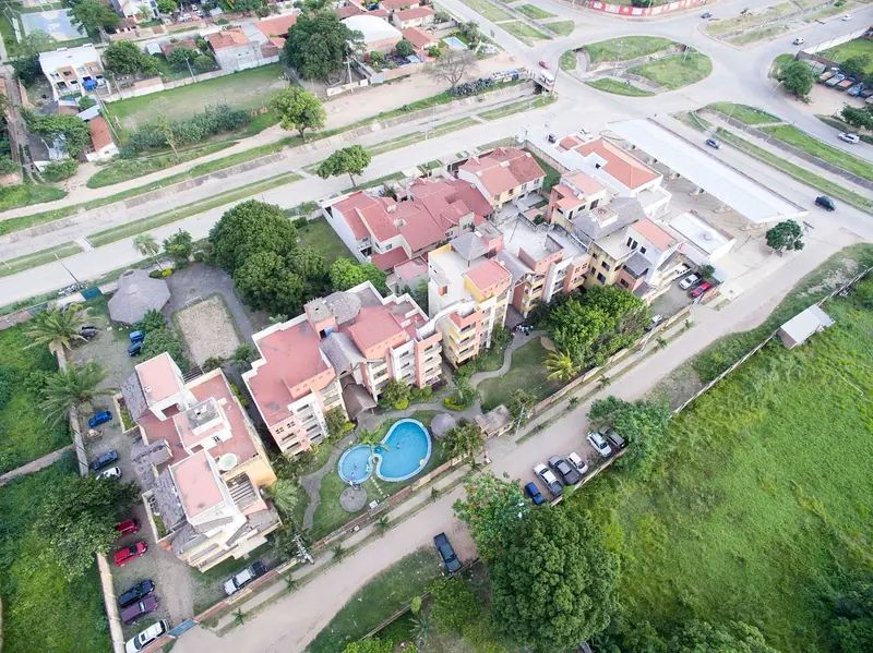 Vista aérea de casas com telhados vermelhos, piscinas e quintais próximos, ao lado de uma área verde