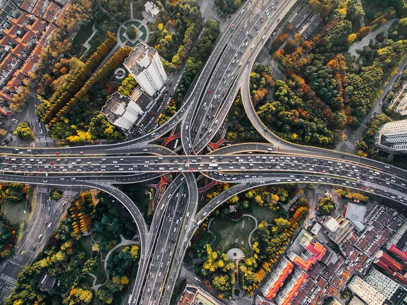 Vista aérea de rodovias e viadutos com carros, cercados de árvores e construções