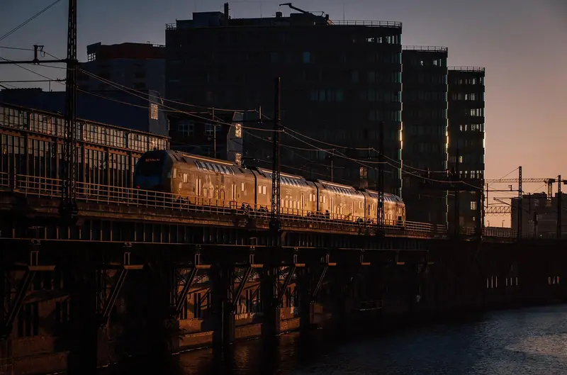 Trem passando sobre um elevado ao entardecer, com prédios da cidade ao fundo