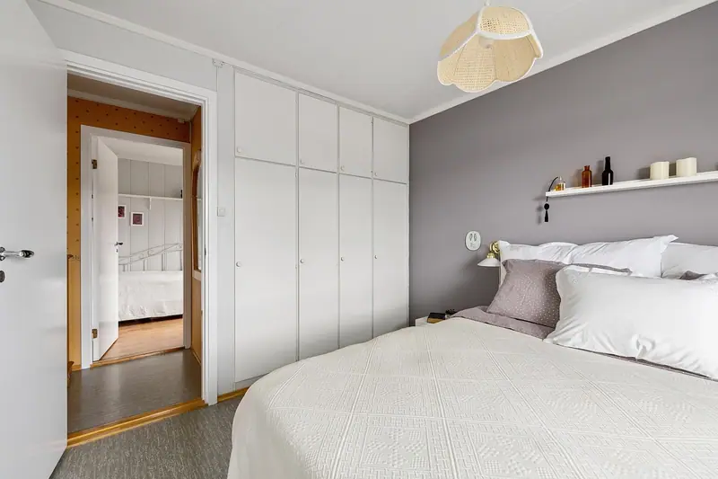 Quarto claro com cama de casal arrumada em branco, parede cinza e armários embutidos