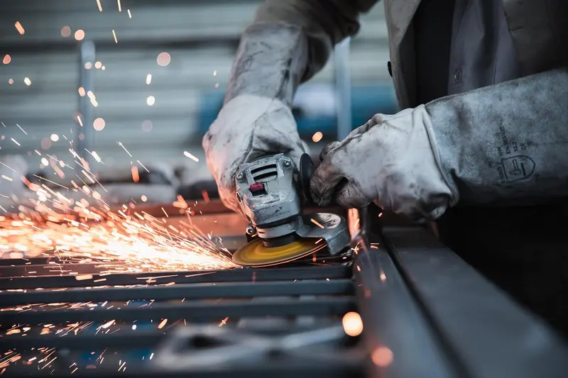 Mãos de luvas usando uma esmerilhadeira que solta faíscas sobre uma estrutura de metal