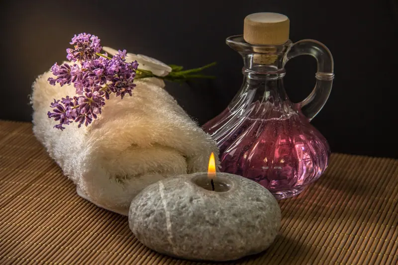 Toalha enrolada com lavanda, vela acesa sobre uma pedra e frasco de óleo sobre bancada de madeira