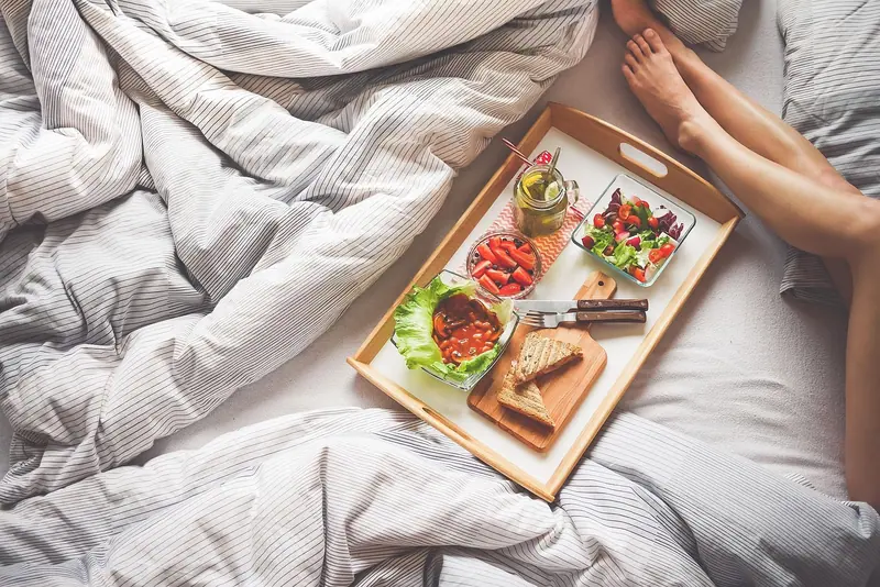Bandeja de café da manhã sobre a cama desarrumada, com os pés de uma pessoa ao lado