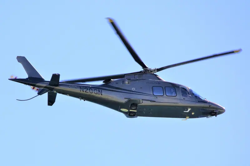 Helicóptero cinza voando num céu azul, visto de baixo