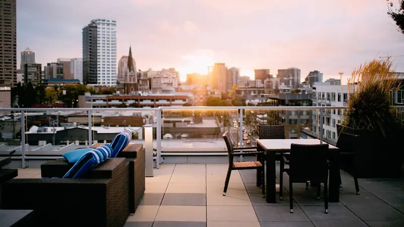Terraço de cobertura com sofá, mesa e plantas, com prédios da cidade ao fundo no fim da tarde