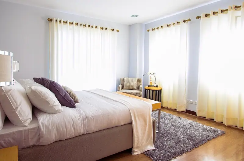 Quarto com cama de casal e janelas largas cobertas por cortinas leves