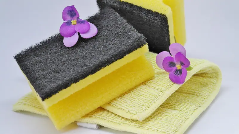 Esponjas amarelas com face verde-escura áspera sobre um pano amarelo, com flores roxas