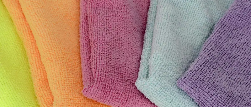 Panos de microfibra laranja, rosa, verde e lilás dobrados lado a lado