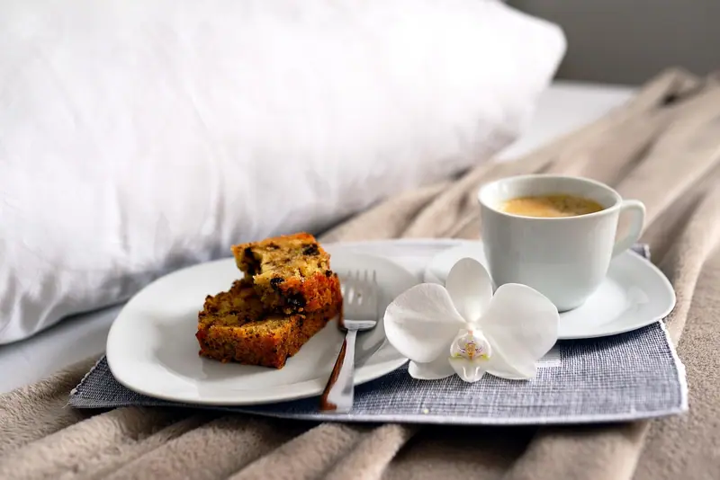 Bandeja com xícara de café, fatia de bolo e uma orquídea branca sobre a cama, de manhã