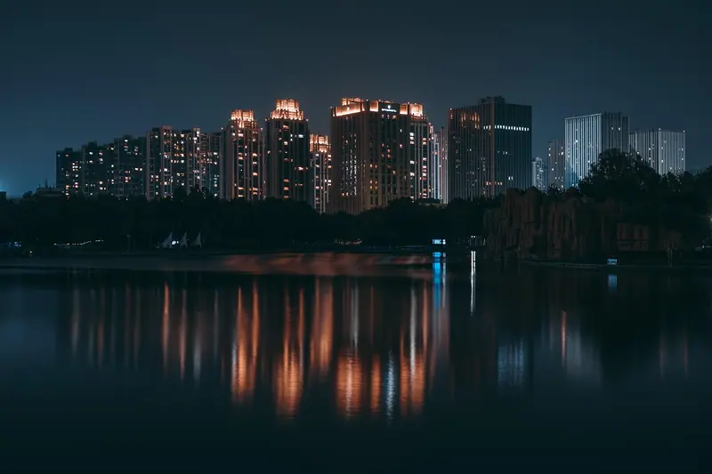 Prédios residenciais com janelas acesas à noite, refletidos na água de um lago