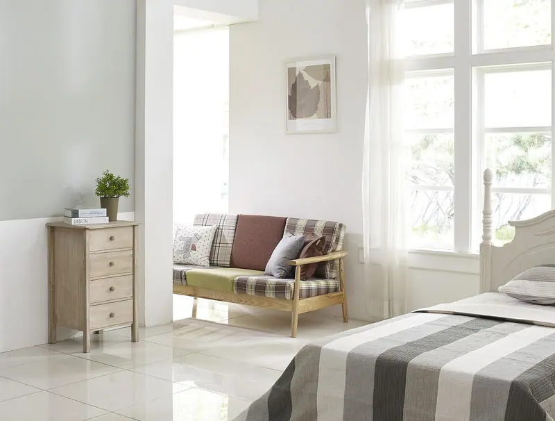 Quarto claro com cama listrada, sofá pequeno e janela grande com cortina branca