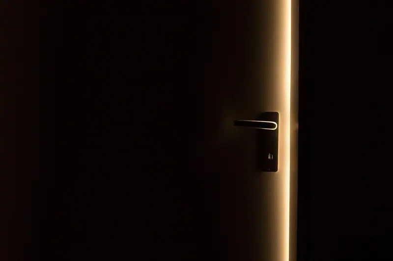 Porta escura levemente aberta, com uma faixa de luz passando pela fresta ao lado da maçaneta