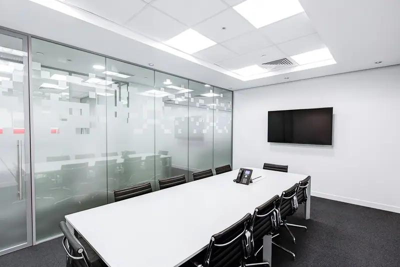 Sala de reunião com mesa branca, cadeiras pretas e divisórias de vidro