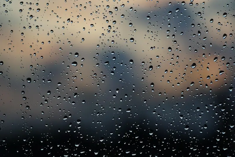 Gotas de água num vidro de janela, com a cidade e o céu desfocados ao fundo