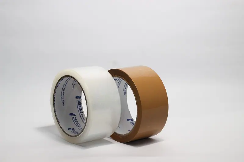 Dois rolos de fita adesiva, um transparente e um marrom, sobre fundo branco