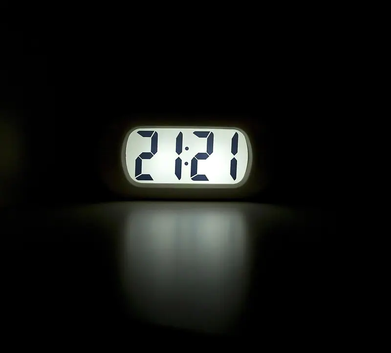 Relógio digital marcando 21h21, aceso num quarto escuro