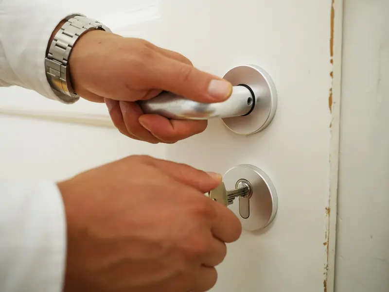 Mãos segurando a maçaneta e girando a chave na fechadura de uma porta branca