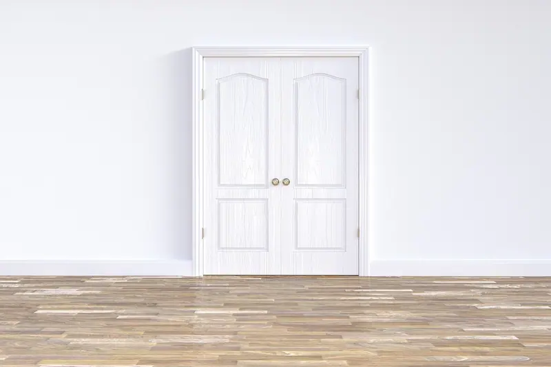 Porta dupla branca fechada numa sala vazia com piso de madeira