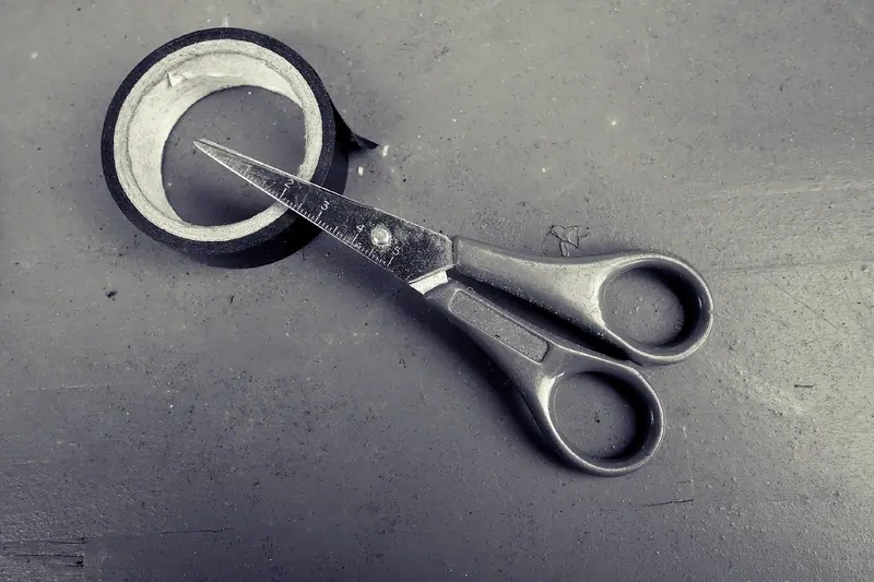 Rolo de fita e tesoura sobre uma superfície cinza