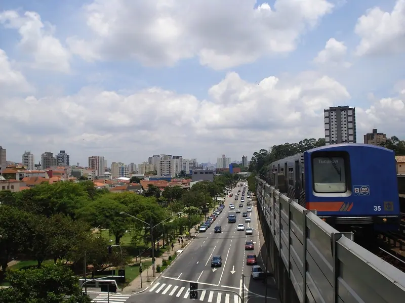 Avenida movimentada em São Paulo com trem passando ao lado e prédios ao fundo