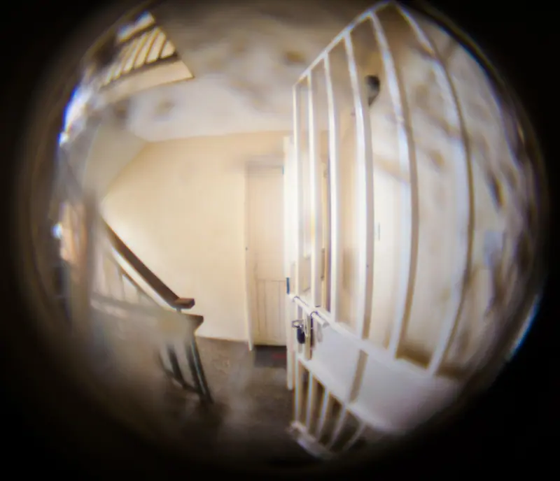 Corredor de um prédio visto pelo olho mágico de uma porta, com a imagem curva